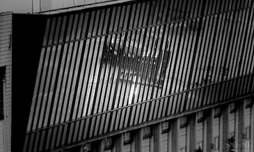 A modern building with slatted exterior design reflecting light through large windows, captured in black and white for a striking architectural photograph.