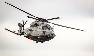 A military helicopter in flight against a cloudy sky, highlighting modern aviation and aerial capabilities. Military helicopter flying in cloudy sky, showcasing advanced aviation technology and dynamic movement.