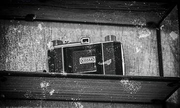 A black and white artistic photo of an old Kodak camera seen through a mirror with weathered textures and splatters. Kodak vintage camera reflected in a mirror with a distressed, grunge aesthetic.