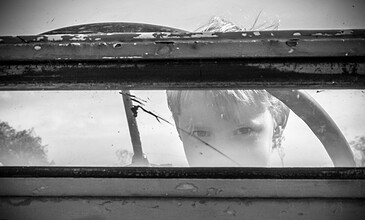 Child looking through a window with a curious expression, black and white photo capturing a moment of wonder and innocence.