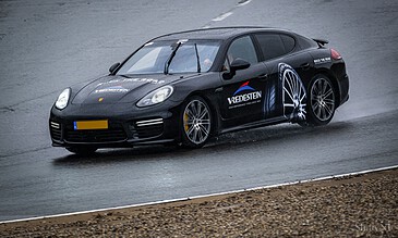 1. High-performance black Porsche sports car racing on wet track, showcasing speed and precision with rain effects and sponsorship decals.