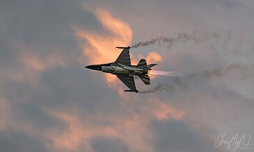 A military jet soaring at high speed against a vibrant sunset sky with clouds, showcasing dynamic motion and aviation expertise. Aero L-39 Albatros jet flying through a colorful sky during sunset, leaving a trail of smoke behind.
