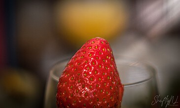 Vibrant close-up of a fresh red strawberry resting on a glass, highlighting the fruit's detailed texture and tiny seeds, perfect for food photography and fruit-focused content.