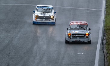 Aerial shot of classic race cars driving on a wet track during a rainy day, showcasing adrenaline and vintage racing excitement.