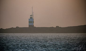 A lighthouse on a rocky coast during sunset with calm waters reflecting the sky.