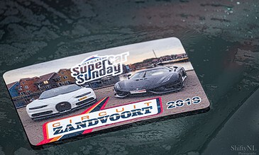 1. Vintage car rally souvenir card featuring Ferrari and Lamborghini cars at Circuit Zandvoort, with raindrops on the surface.