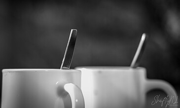 1. Close-up of ceramic mugs with metal spoons on a dark blurred background, black and white shot emphasizing textures and reflections.