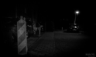 A nighttime photo showing parked cars, a streetlamp, and a quiet, dimly lit street capturing serene nighttime moments. A dark night scene of parked cars along a street with a single illuminated streetlamp, creating a moody and atmospheric urban environment at night.