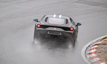 1. A black Ferrari driving on a wet race track during rainy weather, with water spray behind, demonstrating high-speed racing in challenging conditions.