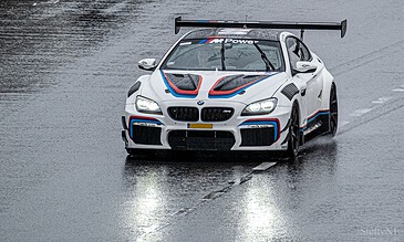 A high-performance BMW race car on a wet track, showcasing precision driving and sleek design in rainy conditions. Perfect for motorsport photography and car enthusiasts.