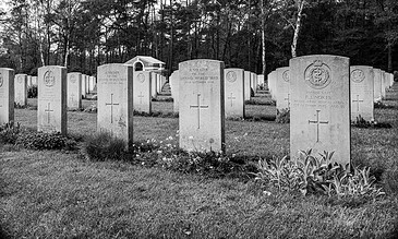 Black and white photograph of a military cemetery with rows of uniform headstones surrounded by trees and grass.