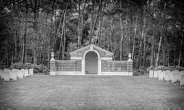 Historic stone monument with a central archway surrounded by a forested area, captured in black and white for a timeless, classic look.