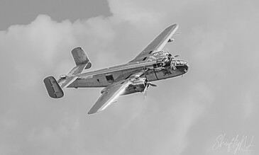 A vintage aircraft soaring amidst clouds, showcasing classic aviation design and engineering. Aero plane flying through cloudy sky, captured in black and white.