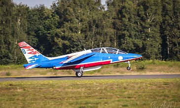 A sleek, blue and white jet aircraft with red accents, captured during takeoff on a clear day, showcasing aviation photography skills. Aero L-39 Albatros jet trainer aircraft taking off from a runway with a forested background.