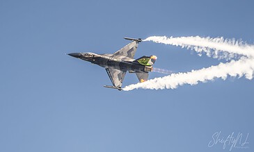 A sleek F-16 fighter jet executing an impressive high-speed maneuver, leaving white smoke trails during an airshow. F-16 fighter jet performing an aerial stunt with smoke trails against a clear blue sky.