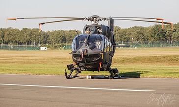 Black helicopter parked on runway with open landscape and trees in the background during daytime.