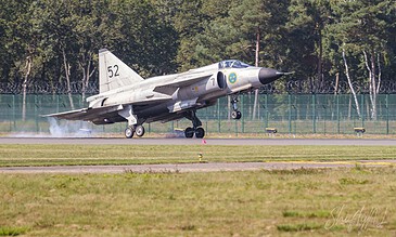A military jet aircraft during takeoff, showcasing sleek design and powerful engines, set against a backdrop of trees and a clear sky. Aero L-29 Delfín jet aircraft taking off from a runway with a forest background.