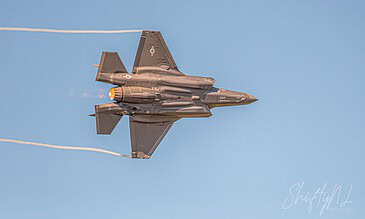 A sleek F-16 fighter jet soaring through the sky during an airshow, showcasing advanced military aviation technology. F-16 fighter jet flying at high speed against a clear blue sky, leaving vapor trails behind.