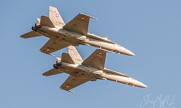 Two Swiss Air Force fighter jets flying in close formation against a clear blue sky, showcasing precision and military aviation skills.
