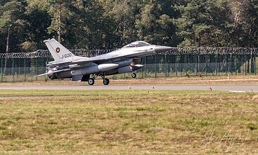 A sleek F-16 fighter jet accelerating on the runway during takeoff, with a backdrop of green trees and a clear sky, highlighting advanced military aircraft. F-16 fighter jet taking off from runway with trees in background, showcasing military aviation.