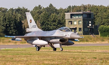 Close-up of a military jet preparing for takeoff on a sunny day, showcasing sleek design and powerful engines. Aero fighter jet taxiing on runway with green trees and a building in the background.