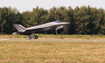 A sleek F-35 fighter jet accelerating on the runway during takeoff, with a backdrop of green trees and a clear sky, highlighting modern aviation technology. F-35 fighter jet taking off from runway with trees in background, showcasing advanced military aircraft in action.