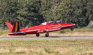 A striking red fighter jet accelerates down the runway during takeoff, capturing the power and precision of military aviation against a backdrop of lush green trees. Red fighter jet taking off from runway with trees in the background, showcasing aviation photography skills.