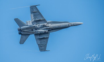 High-speed fighter jet soaring through clear blue sky during an airshow, showcasing sleek design and powerful engines.