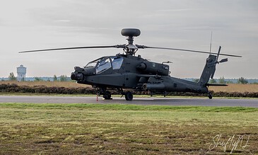 High-tech military helicopter parked on runway with a control tower in the background during daytime.