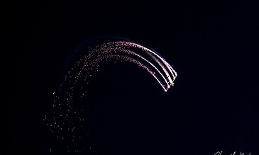 A colorful fireworks display creating a curved trail against a dark night sky, captured in a long exposure shot.