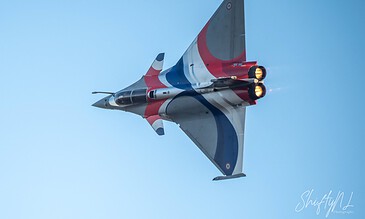 A jet fighter aircraft with a red, white, and blue paint scheme flying at high speed against a clear blue sky.