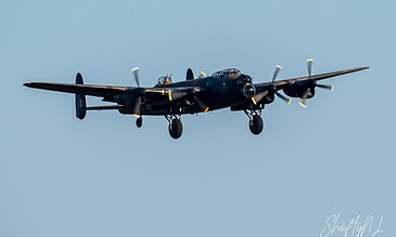 Vintage black propeller aircraft flying in clear blue sky, showcasing classic aviation design and engineering.