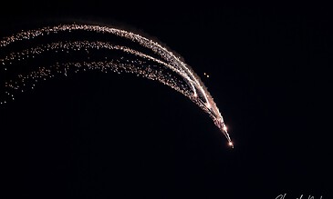 Aero model rocket launching at night with bright trails against a dark sky, captured in motion.