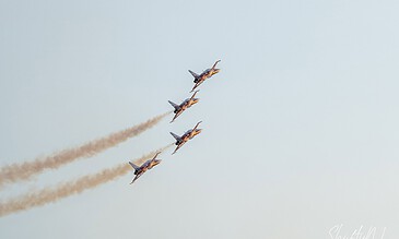 Aero team of four fighter jets flying in tight formation, leaving smoke trails in the sky during an airshow.