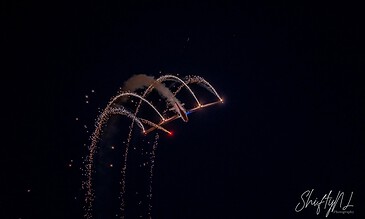 Aerial fireworks display illuminating the night sky with bright, colorful sparks and trails, captured in a macro style by ShiftyNL Photography.
