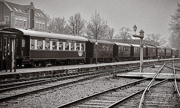 Vintage black and white train with multiple carriages on railway tracks in a historic town setting, capturing nostalgic transportation scenes.