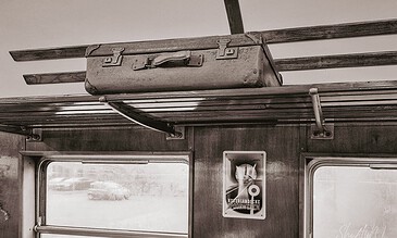 Old suitcases on a wooden luggage rack inside a vintage train car.