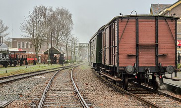 1. Vintage railway station with historical train cars, steam locomotive, and old architecture in a scenic outdoor setting during daytime.
