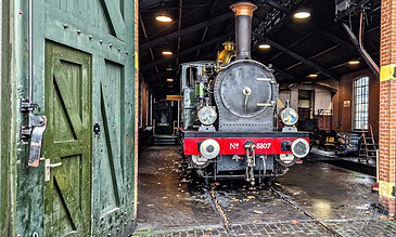 1. Vintage steam locomotive inside a train depot, showcasing historical engineering and industrial architecture.