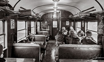 A vintage train car interior in black and white with passengers seated, some engaging in conversation, creating a nostalgic atmosphere of travel moments.