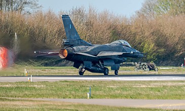 High-speed military aircraft launching on a clear day with vibrant trees in background, capturing dynamic moment of flight. F-16 fighter jet taking off from runway, showcasing powerful engine thrust and sleek design in a vibrant outdoor setting.