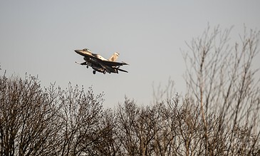 A sleek F-16 fighter jet soaring above winter trees, showcasing advanced military aircraft technology, agility, and power during a flight demonstration. F-16 fighter jet flying low over leafless trees during daytime, capturing a dynamic moment in aviation and military training.