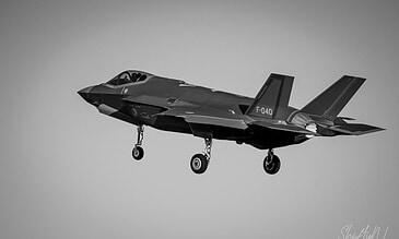 Striking black and white image of an F-35 fighter jet soaring through the sky, highlighting precision engineering and modern military aircraft capabilities. F-35 Lightning II fighter jet in mid-flight, showcasing advanced stealth technology and aerodynamics in a black and white photo.