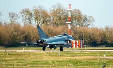 Close-up of a sleek military fighter jet preparing for takeoff on an airfield with background scenery of trees and communication tower. Euro fighter ready for take off on runway with trees and airport tower in background, captured in vibrant colors and sharp detail.