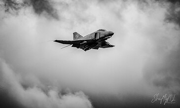 F-4 Phantom fighter jet flying through cloudy sky in black and white image, showcasing military aviation and aircraft photography.