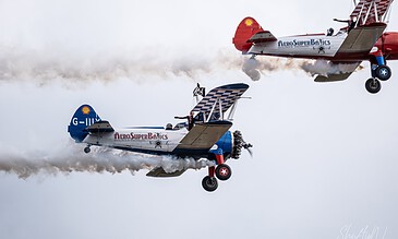 AeroSuperBatics formation flying stunt planes performing an impressive mid-air stunt with smoke trails against a cloudy sky.