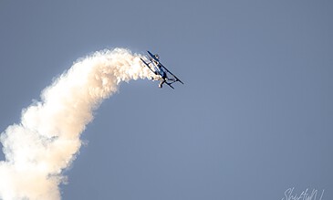 Stunt plane performing aerobatics with a trail of white smoke against clear blue sky, capturing thrilling moments of aviation skills and aerial spectacle.