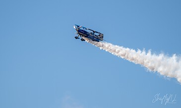 Aviation stunt plane performing in the sky with white smoke trail during an airshow.