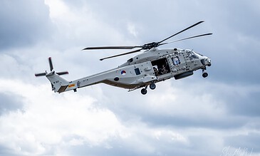Eurocopter helicopter flying in cloudy sky, military aircraft with open door showing personnel inside, high-quality aviation photography capturing movement and technical details, perfect for showcasing aerial capabilities and military operations.