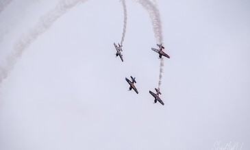 Jet aerobatic planes performing an aerial stunt with smoke trails in the sky during an airshow.